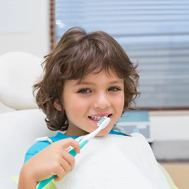 A child brushing their teeth while sitting in a dental chair
