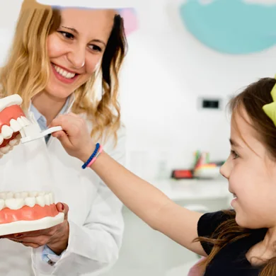 A member of the dental team showing a young patient how to brush, using a model of the teeth